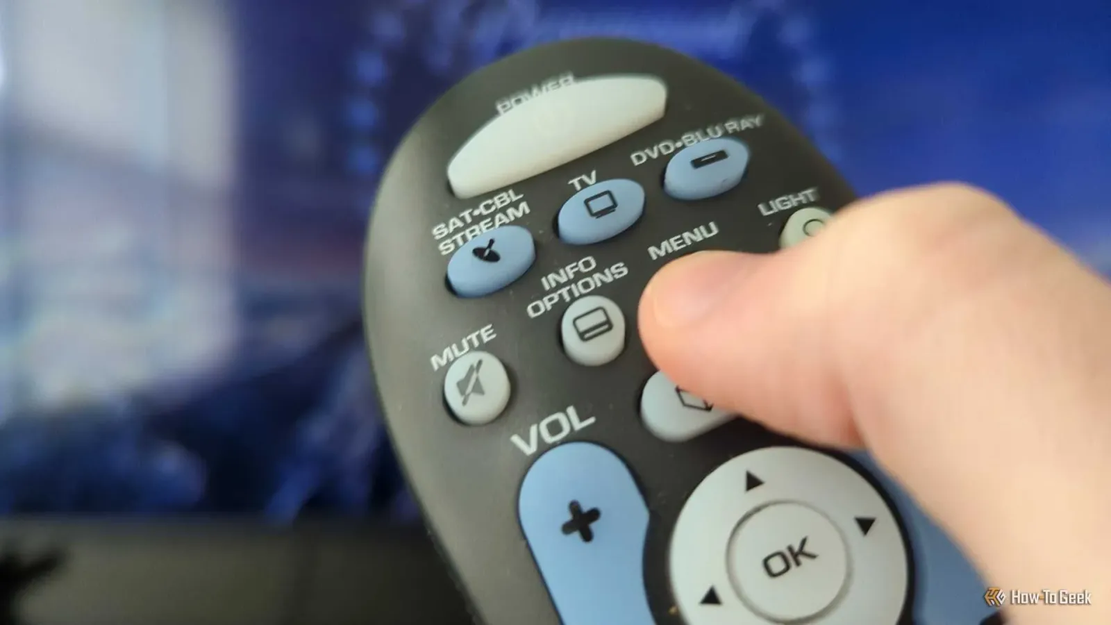 Person's thumb on the Menu button on a universal remote control.
